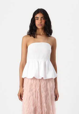 Top peplum alb fără bretele, realizat dintr-un material neted, cu un tiv evazat. Purtați cu o fustă texturată roz.