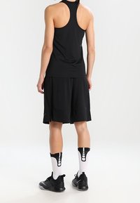 Schwarzes ärmelloses Sportoberteil kombiniert mit lockeren schwarzen Shorts, getragen mit schwarzen Turnschuhen und weißen Socken mit einzigartigem skeletthaltigem Design.