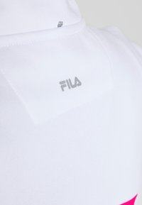 White athletic hoodie with a textured fabric, featuring a subtle Fila logo in silver and a bright pink accent at the bottom.