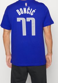 Modré bavlněné tričko s velkým bílým textem "DONČIĆ" a číslem "77" ve stříbrném vzoru na zádech. Krátké rukávy, design s kulatým výstřihem.