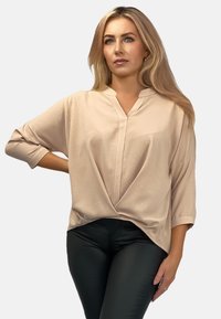 Jasnobiała bluzka z dekoltem w serek i rękawami do łokcia, z przodu z węzłem. Połączona z czarnymi, dopasowanymi spodniami.