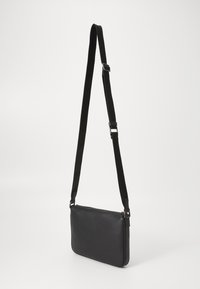 Black crossbody bag made of smooth material, rectangular shape, adjustable strap, zip closure, minimalistic design.