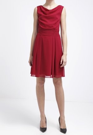 Czerwona sukienka bez rękawów z dekoltem typu kaptur, dopasowanym górnym krojem i rozkloszowaną spódnicą. Wykonana z lekkiego materiału z marszczeniami w talii.