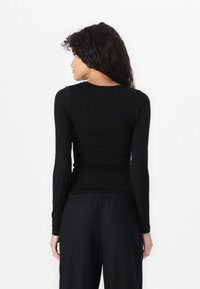 Crna majica dugih rukava s prilagođenim krojem, okruglim izrezom i glatkom teksturom. Uparena s širokim crnim hlačama.