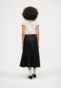 Fustă din denim negru, cu formă A-line și detaliu cu fermoar pe spate, asociată cu un top de culoare deschisă și sosete tricotate albe, purtată cu pantofi negri.