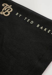 Sort stof med guld broderet "TB" logo og guldtrykt tekst "BY TED BAKER" på en hvid baggrund.