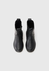 Botas de tobillo de cuero negro con superficie lisa, punta redonda, cremalleras laterales y tiradores en el talón para facilitar el poner y quitar.