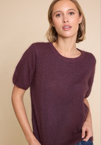 Kortermet genser laget av myk, teksturert stoff i en dyp burgunderfarge. Har rund hals og avslappet passform.