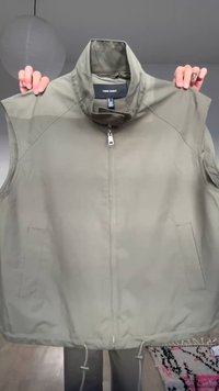 Olivengrønn ermeløs vest med frontglidelås og lommer, holdt opp med hender som viser en høy krage og justerbare snorer ved kanten.