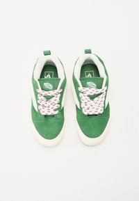 Grønne semskede sneakers med hvide accenter, med snørebånd i pink og hvid blomsterprint og et logo på tungen, minimalistisk design.