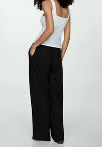 Débardeur ajusté blanc et pantalon noir large et ample avec poches latérales ; texture lisse et design simple sans embellissements.