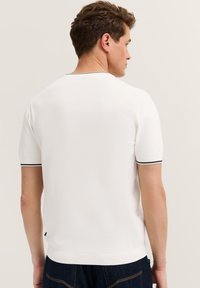 Kurzärmliges weißes Poloshirt mit schwarzem Besatz am Kragen und den Bündchen, aus einem glatten, strukturierten Stoff gefertigt. Rückansicht dargestellt.