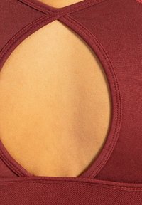 Close-up van een bordeauxkleurige stoffen top met een grote ovale uitsnede die de huid eronder blootlegt.