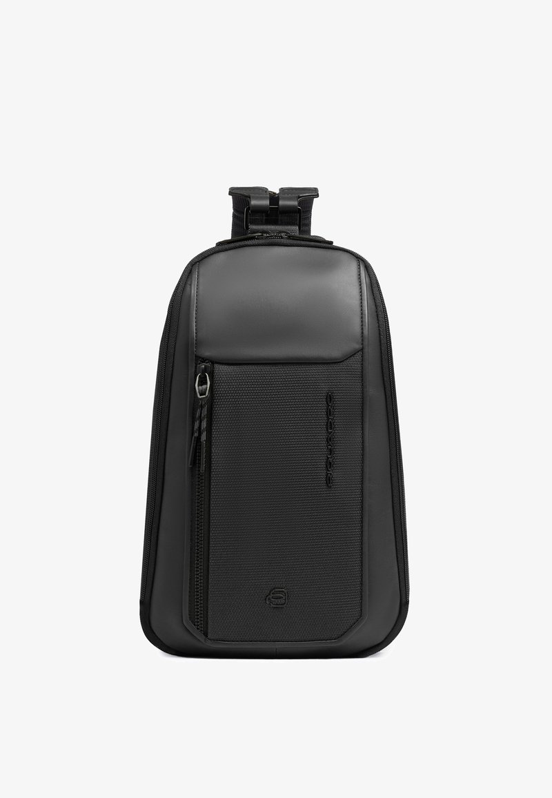 Sac à dos bandoulière noir compact avec panneaux lisses et texturés, poche zippée verticale à l'avant et sangle ajustable en haut.