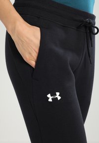 Svarta träningsbyxor med elastisk midja, snörstängning, sidofickor och en vit logotyp på nedre vänstra benet.