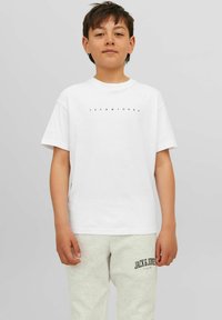 Balta medvilninė marškinėliai su paprastu juodu "JACK & JONES" logotipu ant krūtinės, derinami su šviesiai pilkomis sportinėmis kelnėmis.