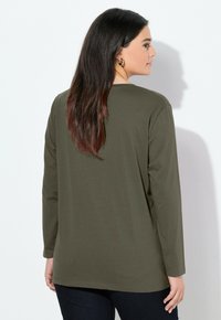 Chemise à manches longues vert olive avec une coupe décontractée, encolure ronde et tissu doux. Coutures visibles le long de l'ourlet et des manches.