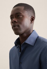 Camicia blu con un motivo a pois; presenta un colletto button-down e un tessuto testurizzato, evidenziando una vestibilità su misura.