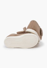 Hellbraune Kleinkinderschuhe mit weißen Gummi-Sohlen, wobei ein Schuh das Sohlenmuster und den Text "Hergestellt in Spanien" zeigt, auf einem weißen Hintergrund präsentiert.