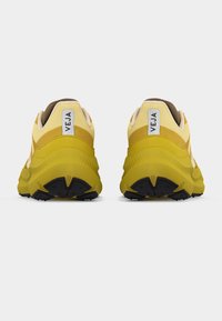 Ζευγάρι κίτρινων και μπεζ παπουτσιών VEJA, εμφανιζόμενα από πίσω, με παχιά κίτρινα πέλματα και μαύρο μοτίβο πέλματος.