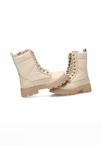 Botas de tobillo beige con un acabado texturizado, diseño con cordones y punta redonda. Presenta una suela resistente con perfil para mayor agarre. Incluye una lengüeta para facilitar el calzado.