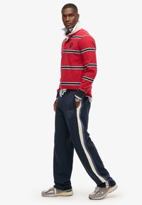 Rød og marineblå stribet rugbytrøje med hvid krave, parret med marineblå sweatpants med sideløb og logo-detaljer. Grå sneakers.