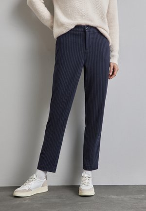 Pantalons rayés bleu marine en tissu doux, avec une coupe droite, une fermeture à bouton, portés avec des baskets blanches et des chaussettes grises.