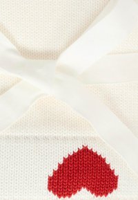 Tessuto a maglia di colore crema con un motivo a cuore rosso e accenti di nastro crema. Texture liscia con un aspetto accogliente, progettato per il calore.