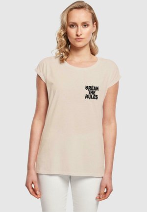 Kortærmet beige t-shirt med et sort teksttryk, der siger "BREAK THE RULES" på venstre brystlommeområde, lavet af blødt bomuldsstof.