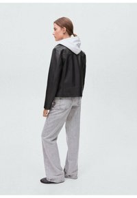 Giacca di pelle nera con una felpa grigia con cappuccio sotto, abbinata a jeans a gamba larga grigi chiari. Design semplice con accenti minimi.
