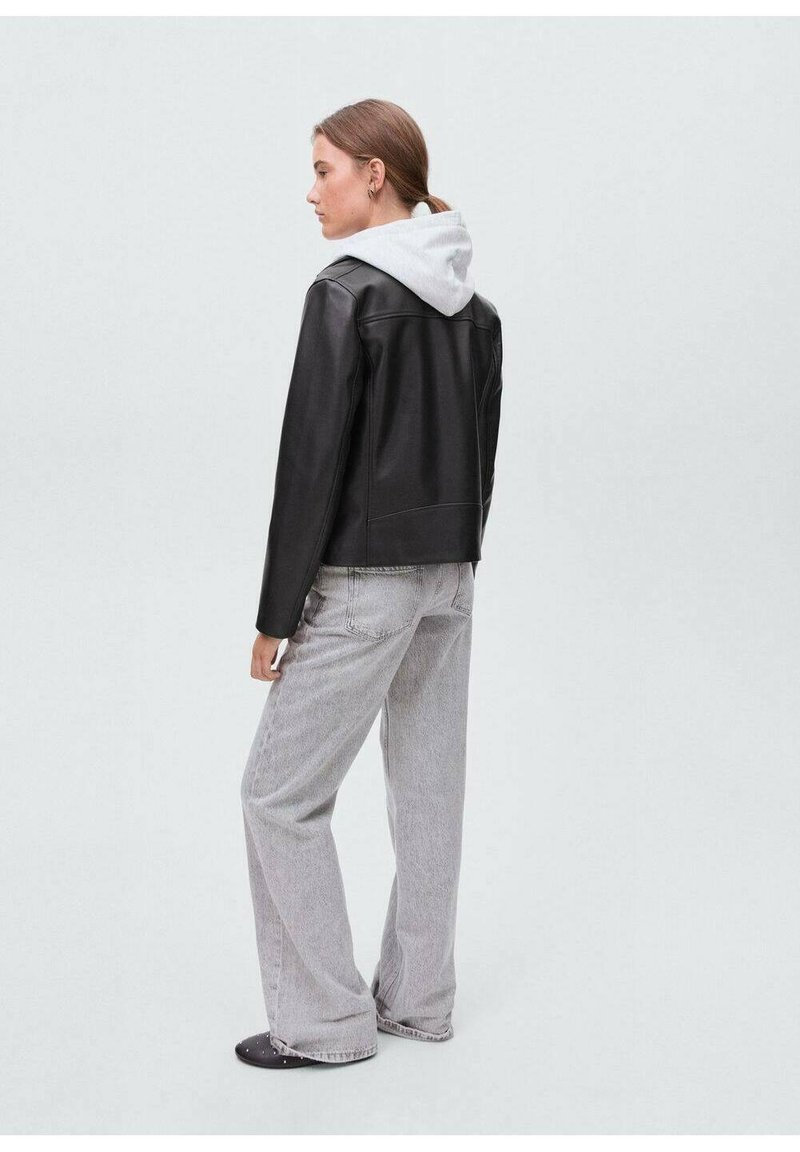 Giacca di pelle nera con una felpa grigia con cappuccio sotto, abbinata a jeans a gamba larga grigi chiari. Design semplice con accenti minimi.