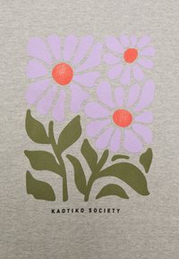 Tre fiori stilizzati di colore viola con centri arancioni e foglie verdi su uno sfondo grigio chiaro, con il testo "KAOTIKO SOCIETY" sottostante.