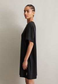 Black short-sleeve dress with a relaxed fit. Made from smooth fabric, featuring a minimalist design and subtle side detail at the hem.