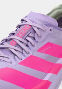 Lila Sport Schuh mit kräftigen pinken Akzenten, strukturiertem Obermaterial, auffälliger Markenkennzeichnung und schlankem Design mit flachen Schnürsenkeln.