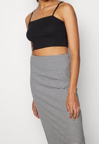 Svart ribbad crop top med tunna band, kombinerad med en figurnära svart och vit houndstooth-mönstrad kjol som framhäver släta texturer.