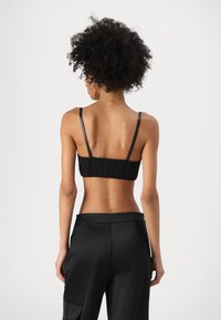 Svart kort bralette med tunna band, slät textur och samlad baksida, kombinerad med högmidjade svarta byxor.