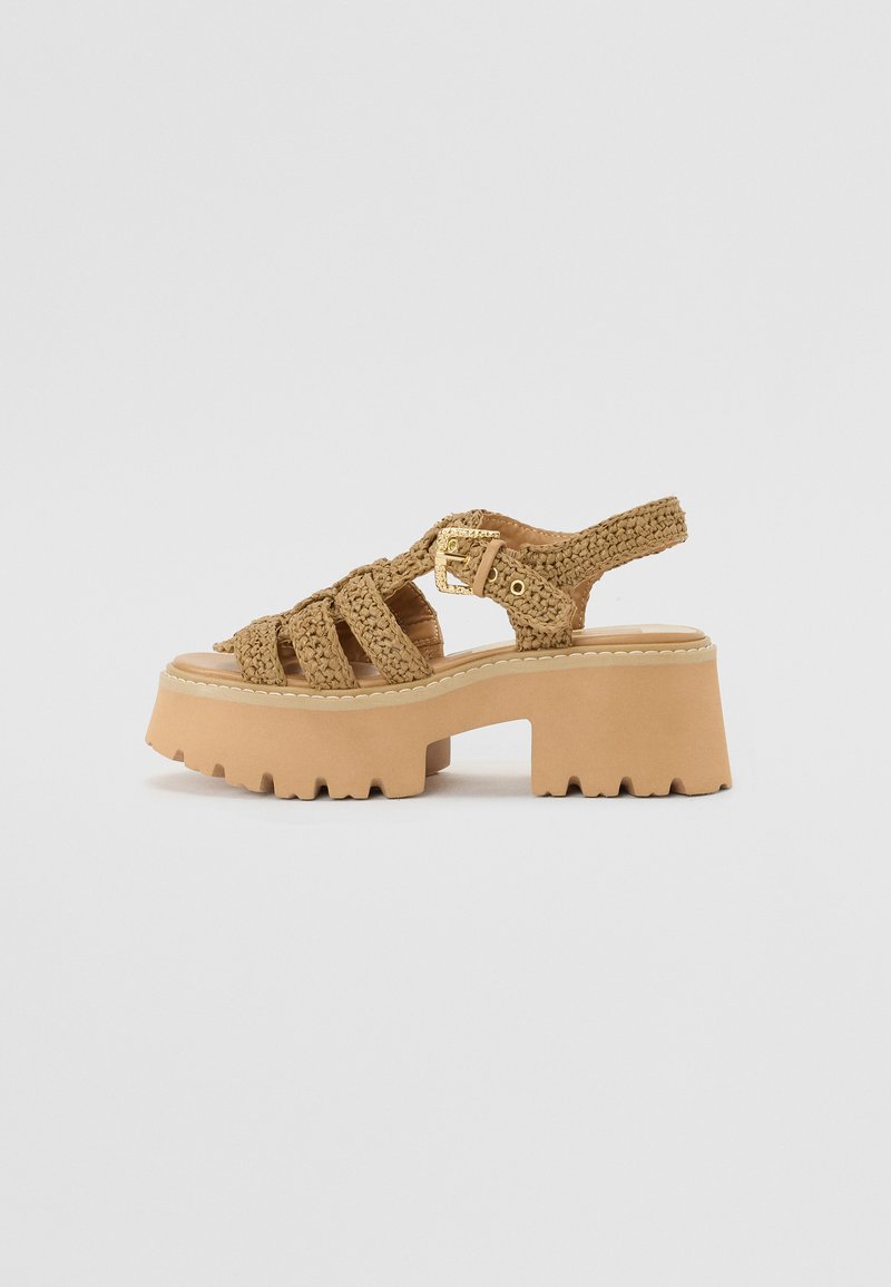 Platform sandalen met een chunky beige zool, geweven banden en een gouden gespaccent voor sluiting. Textuurdetails op de banden.