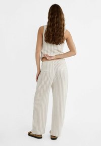 Pruhovaný béžový crop top a široké kalhoty vyrobené z lehkého materiálu. Vlastnosti zahrnují vysoký pas a dvě zadní kapsy. Sandály dokončují outfit.