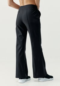 Juodos, platėjančios jogos kelnės su plačiu diržu, pagamintos iš lygaus audinio, su šoninėmis siūlėmis ir nepastebimais kišenėmis.