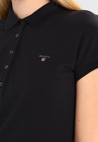 Polo noir en tissu texturé avec un col, doté d'une patte de boutonnage à trois boutons et d'un petit logo brodé sur la poitrine.