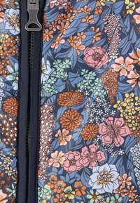 Tyg med blommönster i nyanser av blått, rosa, orange och grönt. Har intrikata blommor och blad samt en central dragkedja.