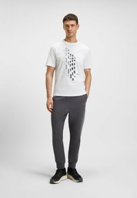 White short-sleeve t-shirt with a geometric black and gray graphic design. Worn with gray sweatpants and black sneakers with a thick sole.