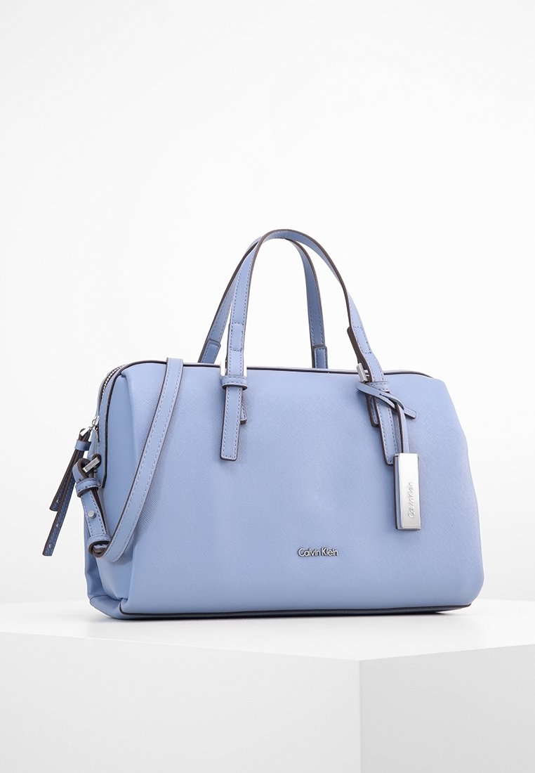 Jasnoniebieska torebka wykonana z teksturowanego materiału syntetycznego. Posiada podwójne uchwyty, srebrne akcesoria oraz odpinany pasek na ramię.