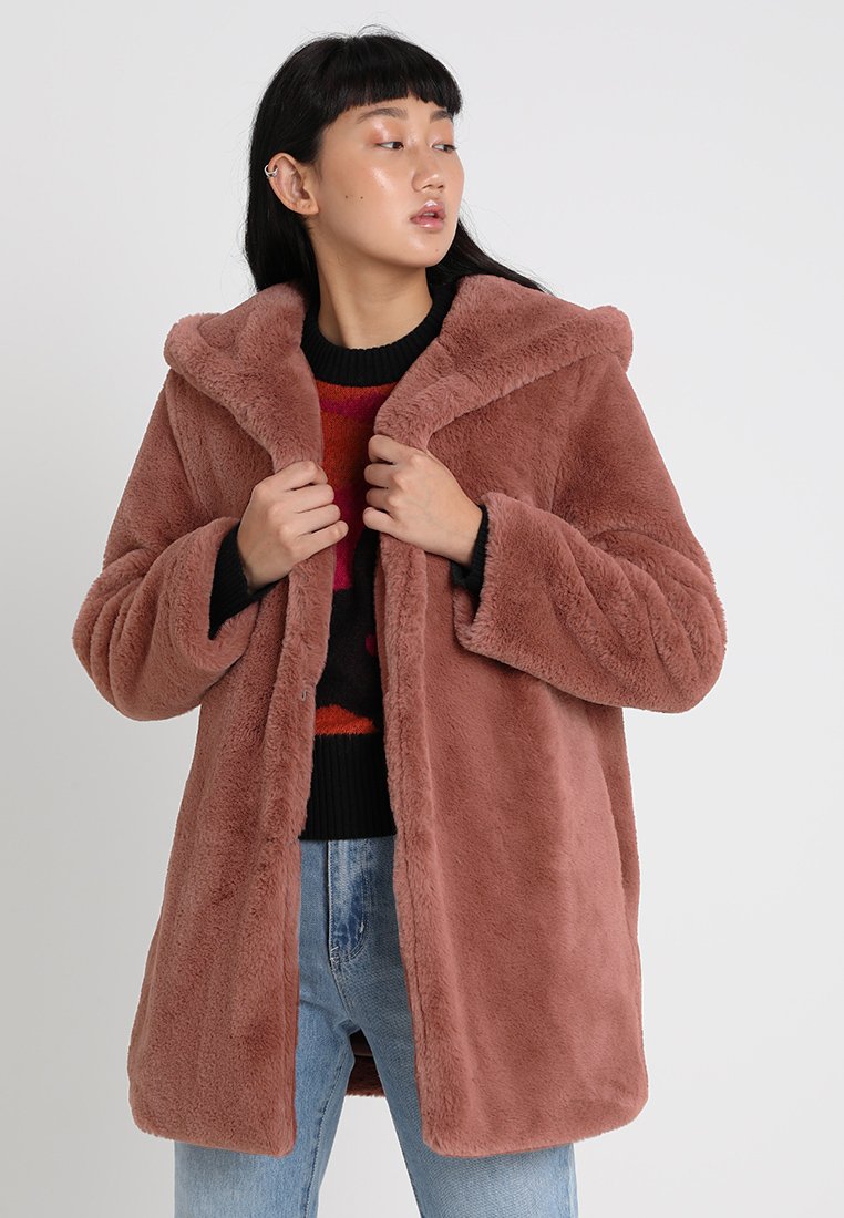 Nepalfleece jas in een stofkleurig rozenkleur, oversized pasvorm, met een capuchon en open voorkant. Heeft een zachte textuur en brede mouwen, gecombineerd met een gebreide trui.