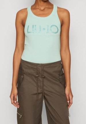 Femme portant un haut côtelé sans manches bleu clair avec le texte "LIU JO" et un pantalon cargo marron avec taille à cordon de serrage et poches zippées.