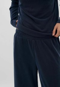 Námornícky modrý súprava na voľný čas obsahujúca voľný top s drapovaným výstrihom a nohavice s elastickým pásom, obidve vyrobené z mäkkej látky.