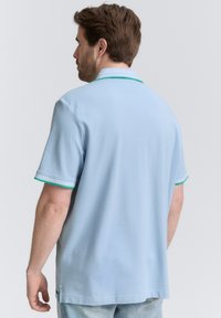 Ljusblå pikétröja med korta ärmar, grön detaljer vid kragen och ärmarna, gjord av mjukt material, med rak passform och sidofickor.