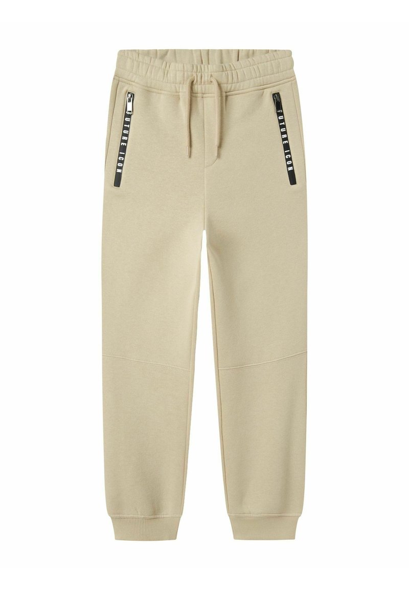 Beige sweatpants tillverkade av mjuk tyg, med dragsko i midjan och två svarta dragkedjefickor på sidorna med tryckt varumärke.
