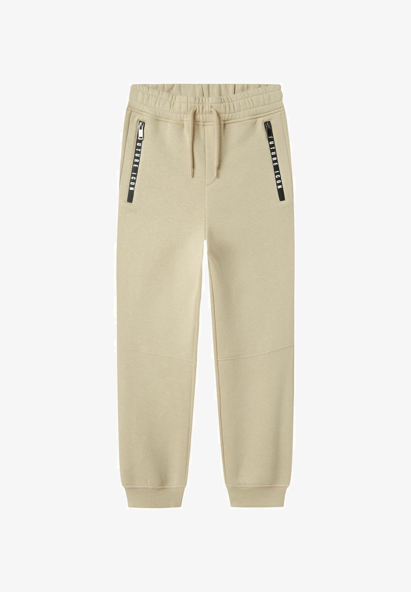 Beige sweatpants gemaakt van zachte stof, met een tailleband met trekkoord en twee zwarte ritssluitingen aan de zijkanten met bedrukte branding.