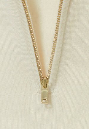 Cream-colored knit fabric features a central gold zipper, highlighting its smooth texture and precise stitching along the edges.